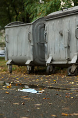 A used mask to protect against coronavirus lies on the asphalt near trash cans. Mask for protection against covid-19. Consequences of covid-19. 