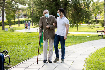Grandfather and grandson spending quality time in park talking and walking with covid masks