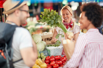 Seller woman selling fresh and organic vegetables at the green market or farmers market stall.  Young buyers choose and buy products for healthy food in grocery.