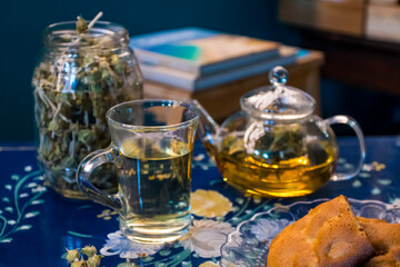 Cup of fresh flower and herb arabic tea and some Tasty and healthy almond cookies, rich in vitamins and less sugar. copy space.Top view on a blue flowers background..