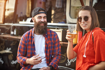 Hipster couple drinking beer in front of food truck; Urban lifestyle concept