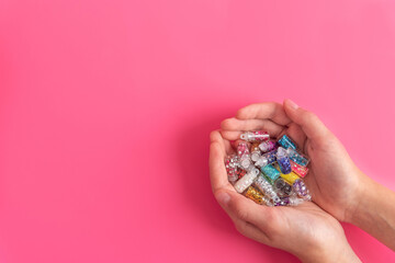 Young woman holding handful with numerous small plastic bottles full of different color glitter for craft works and decoration on pink background close upper view.