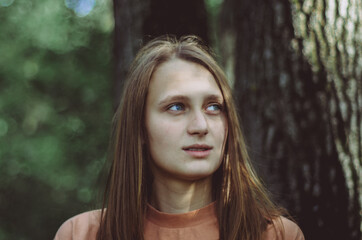 Upper body portrait of a young woman in a forest looking to the side dreamy and wondering