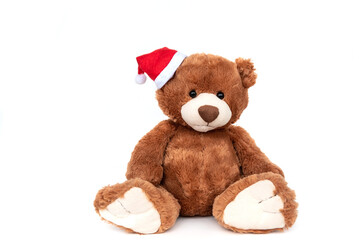 Funny fluffy brown teddy bear best baby stuffed toy with small shiny black plastic eyes wearing Santa Claus red hat in xmas sitting isolated on white background.
