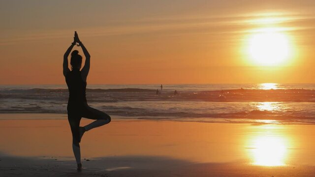 Silhouette of slim woman with arms raised up, Practice of yoga on the beach