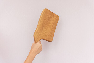 Young woman chef holding stylish clean cutting wooden board in shape of meat cleaver by hand near white blank wall in brightly lit studio close view.