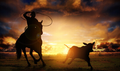 Silhouette of a cowboy riding a horse roping a calf. © ginettigino