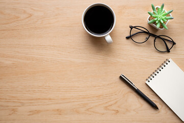 Top view above of Wooden office desk table with blank notebook, pen and coffee cup with glasses. Business and finance concept. Workplace, Flat lay with blank copy space.