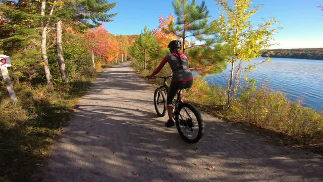 Mountain biking in autumn. Mountain biker riding MTB bicycle on forest gravel path in fall foliage. Video with colorful leaves. Woman living healthy sports lifestyle in fall