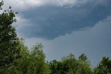 Dark storm clouds and gray gloomy clouds, a terrible natural phenomenon, rain from afar, view from the side