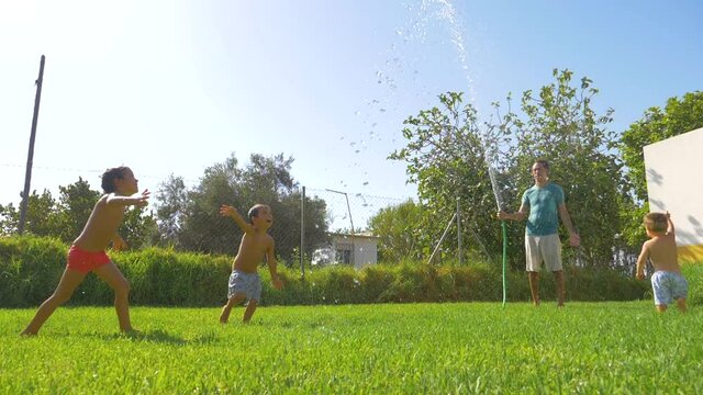 Father playing with his sons in the garden with the hose and water. Watering and playing together in a funny way.