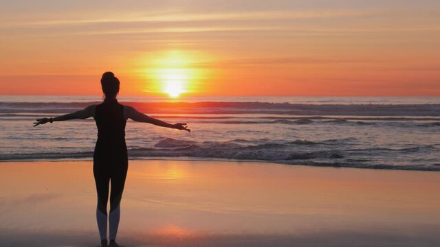 Silhouette of beautiful woman with arms raised up on the beach on golden sand
