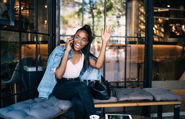 Cheerful woman hailing while talking on phone