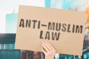 The phrase " Anti-muslim law " on a banner in men's hand with blurred background. Equality. Legislation. Law. Policy. Rules. Protest. Illegal. Ban. Restrictions. Equal