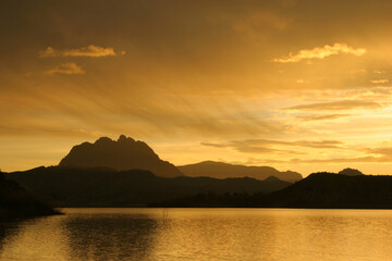 Fototapeta premium Amanecer en un pantano, con montañas al fondo y cielo con nubes. Pantano del Quípar, Calasparra (Murcia).