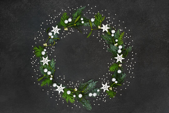 Christmas & solstice wreath with star & silver ball decorations, mistletoe & cedar cypress fir on grunge grey background. Xmas decoration for the festive season.

