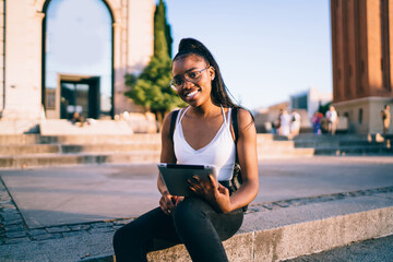 Happy young ethnic lady browsing tablet on street