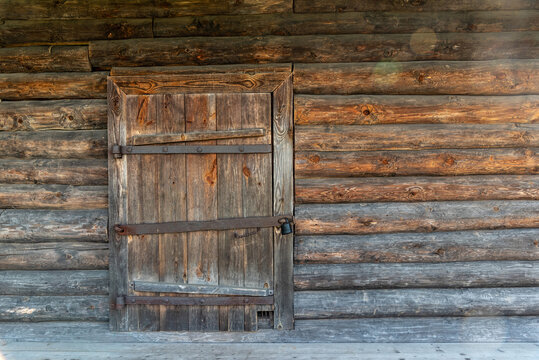 Wooden door of old rural barn locked with large padlock made of withered grey and brown planks and logs in country house yard on autumn day bokeh effect.
