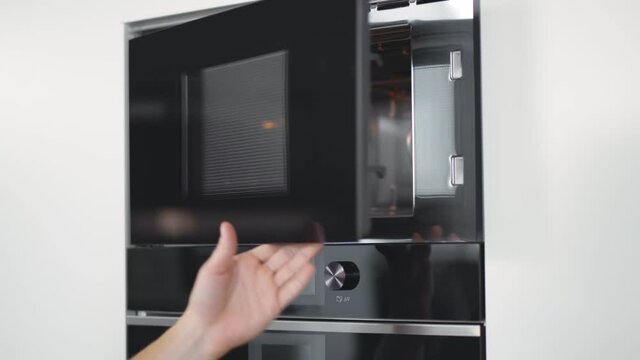 Close up of young man setting microwave oven timer warming food in modern kitchen.