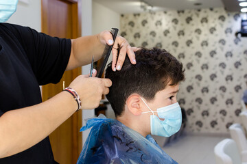 Niño con mascarilla en la peluquería mientras le cortan el pelo 