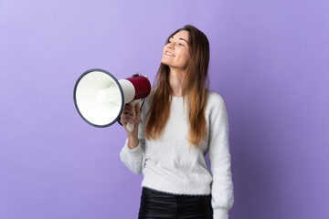 Young Ireland woman isolated on purple background holding a megaphone and looking up while smiling
