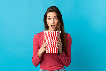 Young Ireland woman isolated on blue background holding a big bucket of popcorns