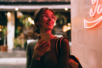 Trendy woman with smartphone on street in neon light - obrazy, fototapety, plakaty