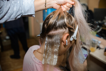 Fototapeta premium The master hairdresser dyes the hair of a young woman, blonde. Home beauty salon. 
