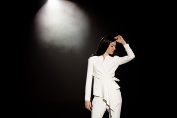 beautiful girl in a white pantsuit on stage in the beam of light