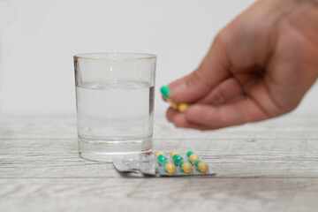 Man's hand holds capsules, next to a glass of water on a wooden table