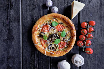 Hot homemade pizza with tomatoes, mushrooms, mozzarella, sweet pepper and Basil on a black background. Snack. Pizzeria. Horizontally.Copy space.