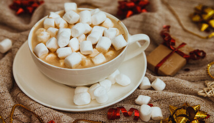 Coffee with marshmallows on a background of knitted fabric with gifts and holiday bows. Cocoa and cappuccino.