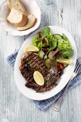 Grilled pork steak with fresh salad. Bright wooden background. Top view. 	