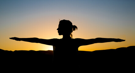 Silhouette of a woman against a beautiful sunset background. a Woman stretches her hands and doing yoga meditation exercise.