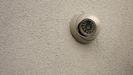 A modern, dome style, infrared IR security camera is shown mounted on a building exterior wall, with room for text or copy space to the left.