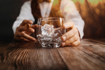 Bartender in a dark leather apron puts three glasses of whiskey on a dark wooden bar in a nightclub. Close-up. Spa ce