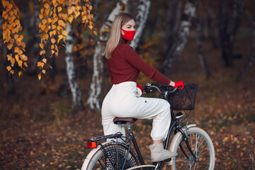 Fototapeta na wymiar Young woman riding bicycle in red gloves and face mask at autumn park