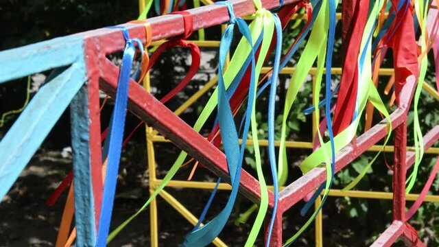 Colorful satin ribbons tangled to kids playground fence and swing in wind. Summer fun background of ribbon decoration outdoor