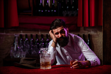 Drunk man sitting at the counter in a pub or a bar and drinking cognac or whiskey. Scotch and cognac.