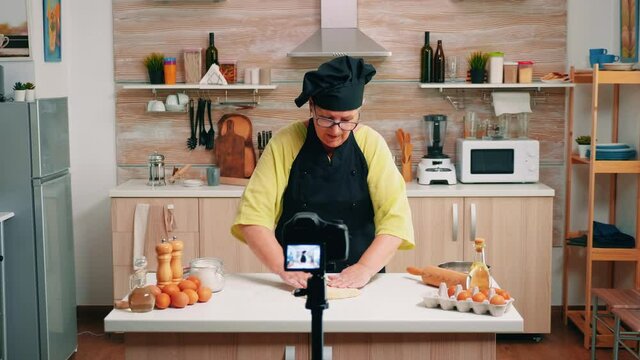 Aged female vlogger making social media video about cooking for the internet channel. Retired blogger chef influencer using technology communicating, shooting blogging with digital equipment