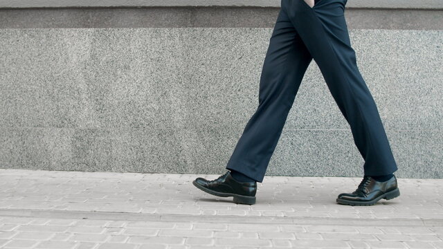 Cropped image man walking in black shoes. Closeup male feet going near building