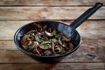 Closeup of a pan of mushrooms with parsley and garlic, on a white rustic wooden board-