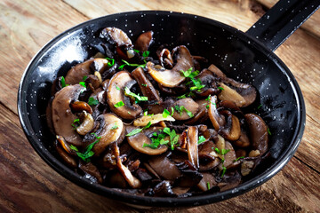 Closeup of a pan of mushrooms with parsley and garlic, on a white rustic wooden board-