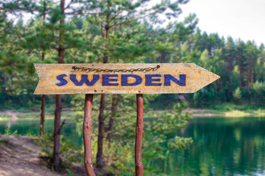 Sweden wooden arrow road sign against lake and pine trees background. Travel to Sweden concept.