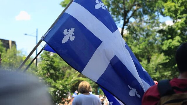 Rear view of young red-haired woman holding quebec country flag waving high in air while standing in protest against public health guidelines