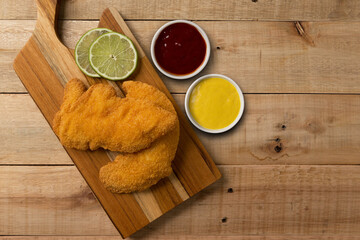 breaded chicken filet, served with mustard and ketchup, on a wooden background. top wiew
