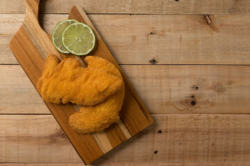 Obraz na płótnie Canvas breaded chicken filet with lemon slices, on a wooden background. top wiew
