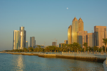 Fototapeta na wymiar The view of the Corniche boulevard with high rises and palm trees on sunset in Abu Dhabi, United Arab Emirates