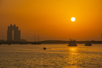 Magical orange sunset in Abu Dhabi with building and boat silhouettes, United Arab Emirates