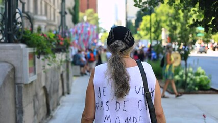 Rear view of senior female walking on footpath towards rally with message on dress regarding protest against public health guidelines